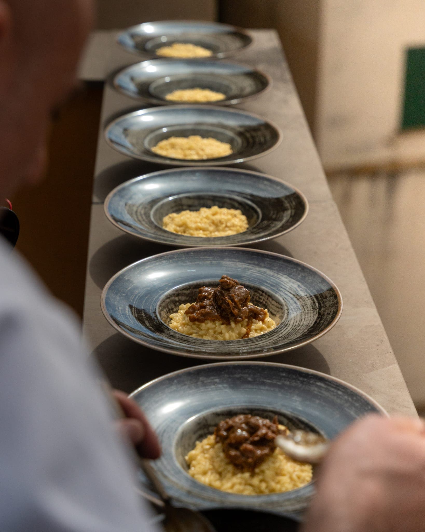Mise en place: fila di piatti di risotto allo zafferano e guancia pronti per il servizio